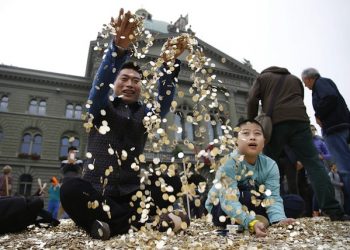 epa03895861 Chinese tourists from Shanghai play in a pile of coins after activists dumped a truck load of 8 Million five-centime coins - representing one coin for every person living in Switzerland - at the Federal Square in front of the parliament building in Bern, Switzerland, 04 October 2013. The about 15 tons of money are worth 400,000 Swiss Francs. At the same time the required signatures for the ''National Initiative for a Unconditional Basic Income' were delivered to the Swiss government.  EPA/PETER KLAUNZER