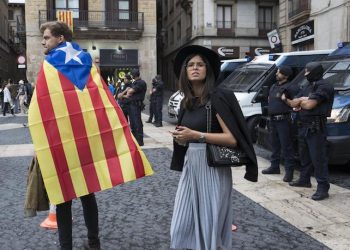 epa06238031 A couple with a Catalonian flag near Spanish police in the Placa Sant Jaume, or the Town Hall Square, in Barcelona, Spain 01 October 2017. Catalonia is holding an independence referendum which has been declared illegal by the Spanish Constitutional Court.  EPA/JIM HOLLANDER