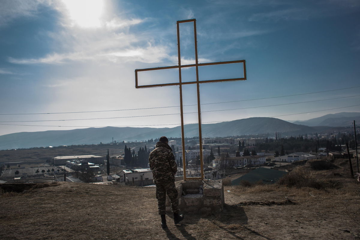 Soldato armeno prega davanti a una croce a Martakert, Nagorno-Karabakh